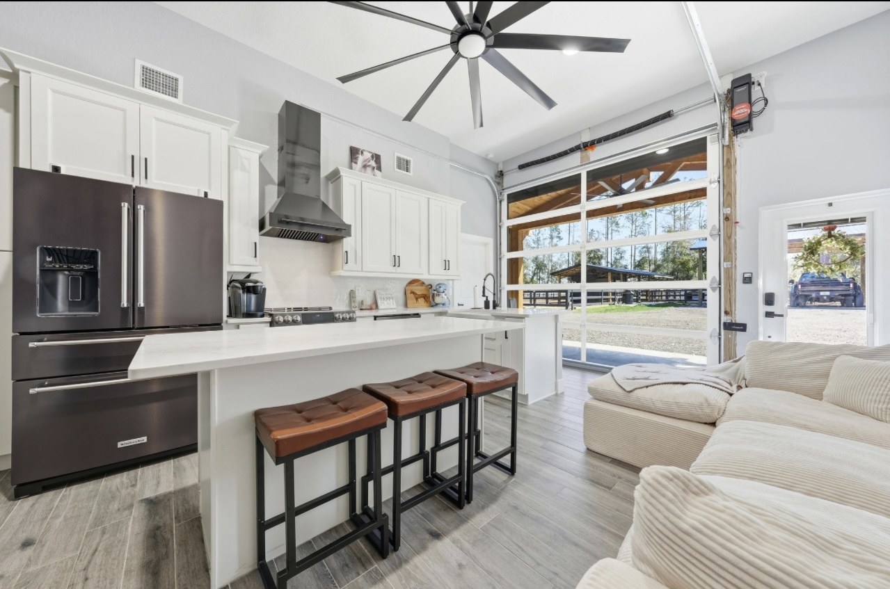 White kitchen with quartz island, leather barstools and an open glass garage door to a covered patio