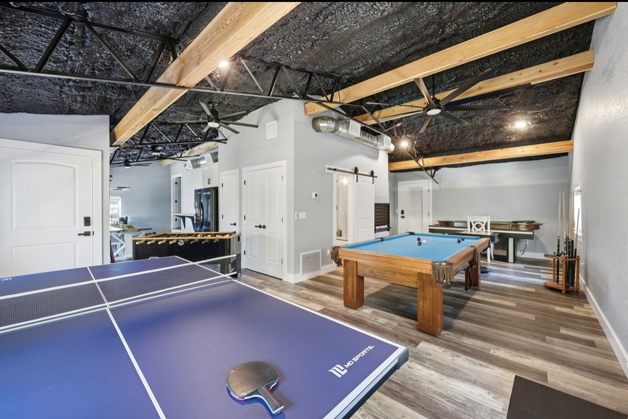Game room with a pool table, ping pong table and exposed truss ceiling with wood beams