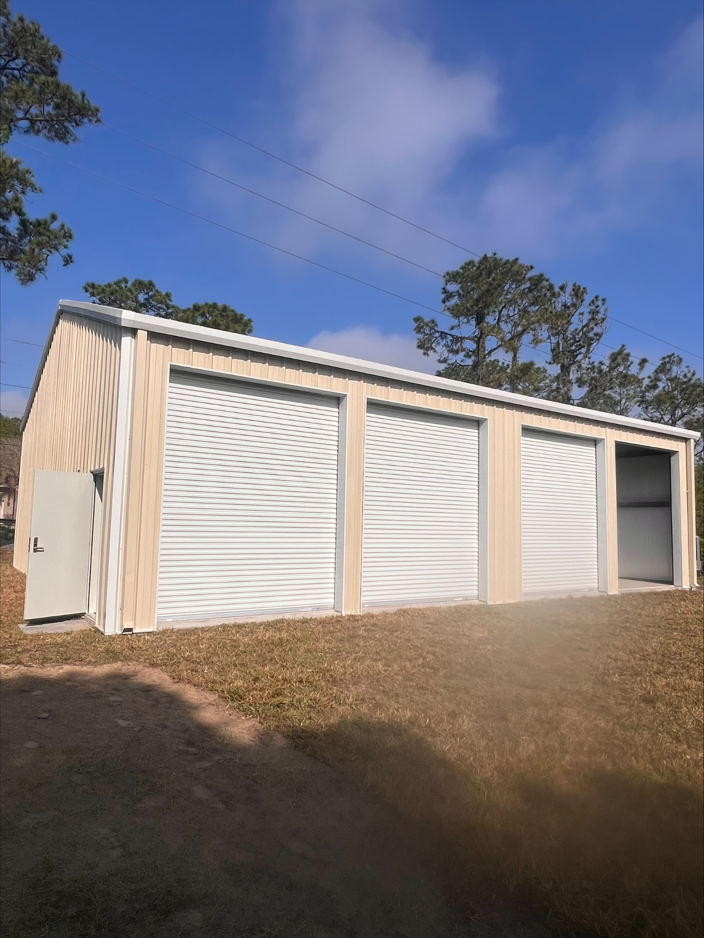 New tan steel building with three white roll-up doors and a walk-in service door