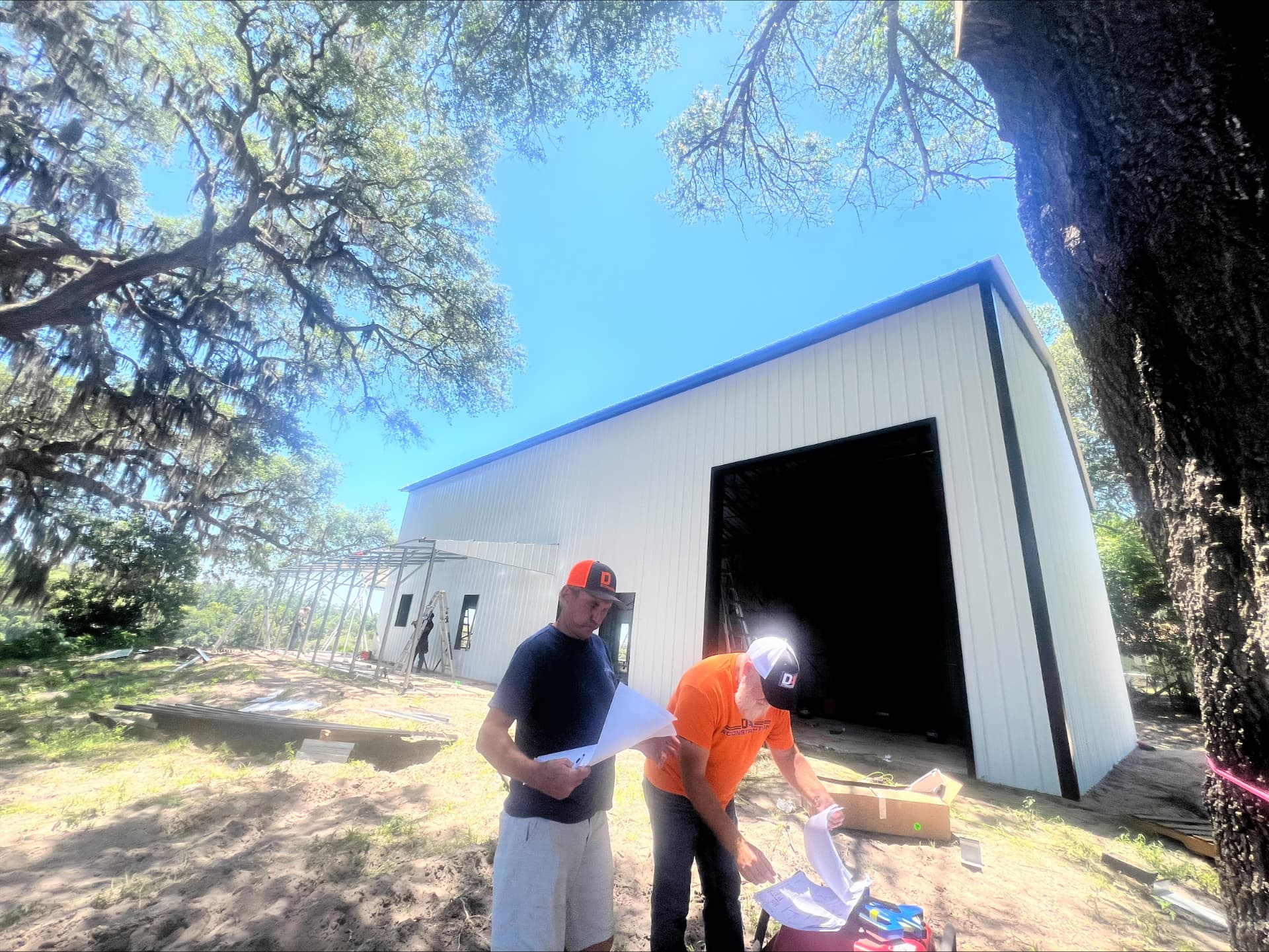 DA Construction team reviewing plans on site in front of a white metal building with a tall bay opening