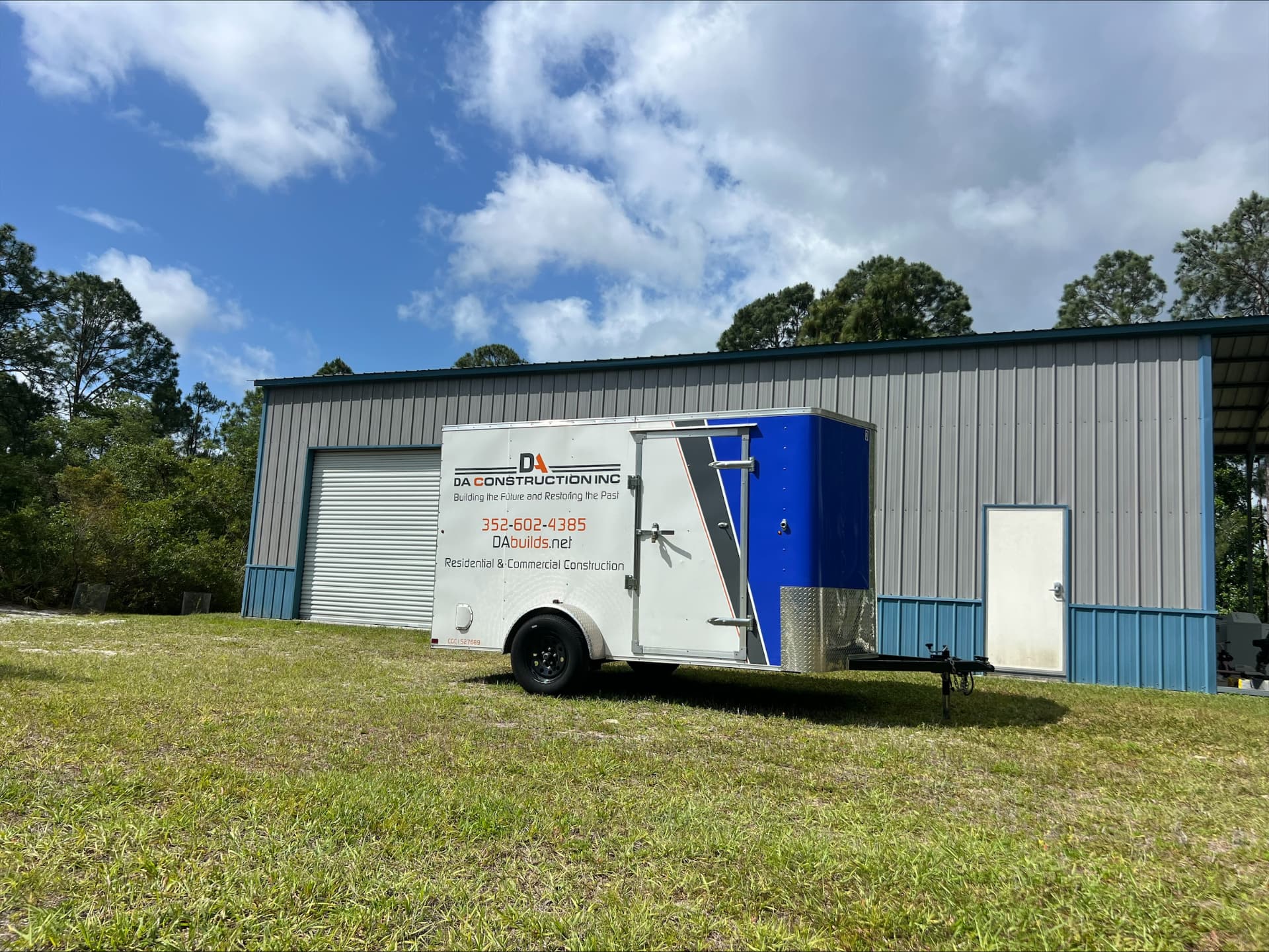 DA Construction branded enclosed trailer parked outside a gray metal shop building