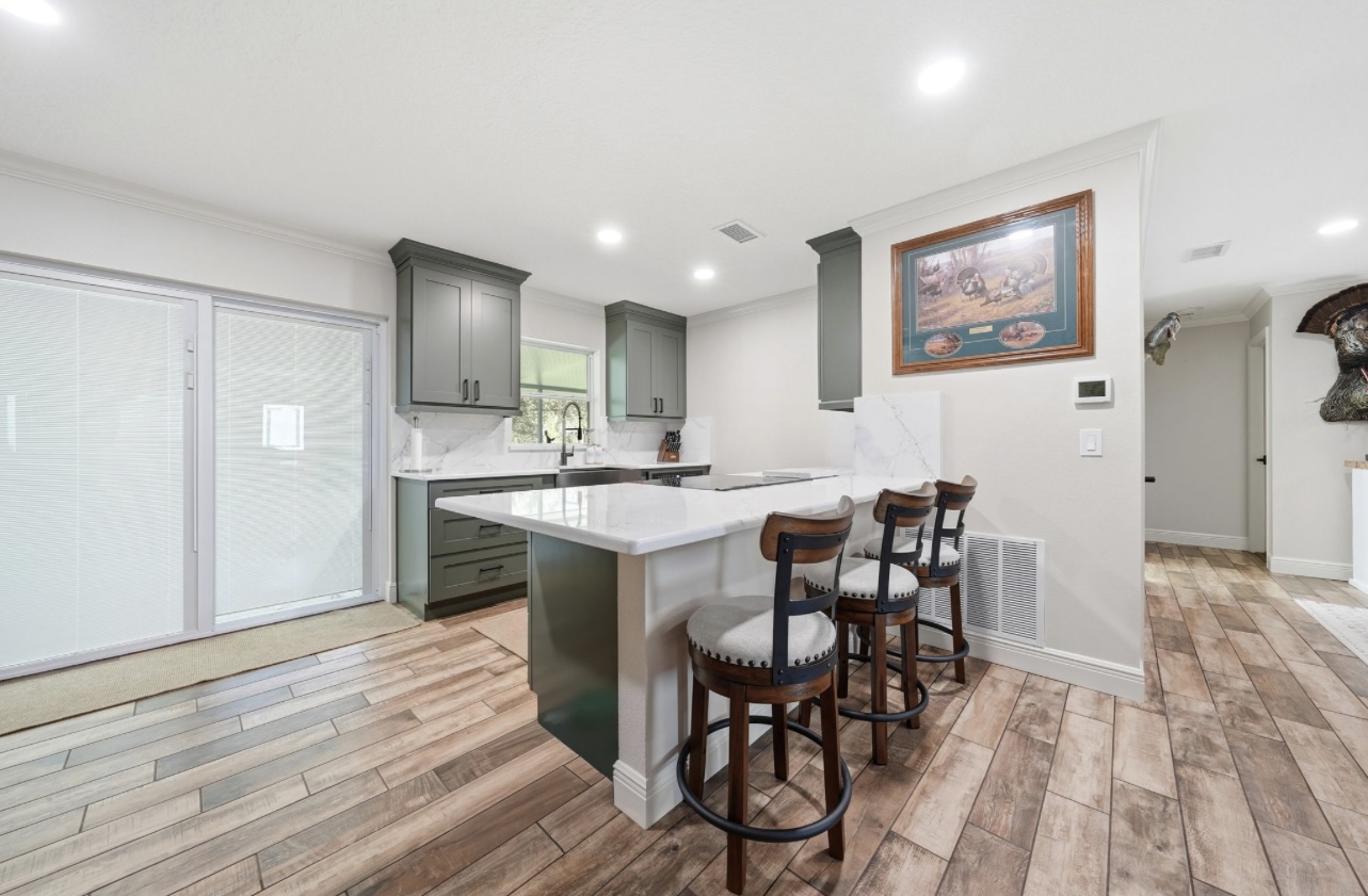 Kitchen breakfast bar with three swivel stools, quartz counter and wood-look tile flooring
