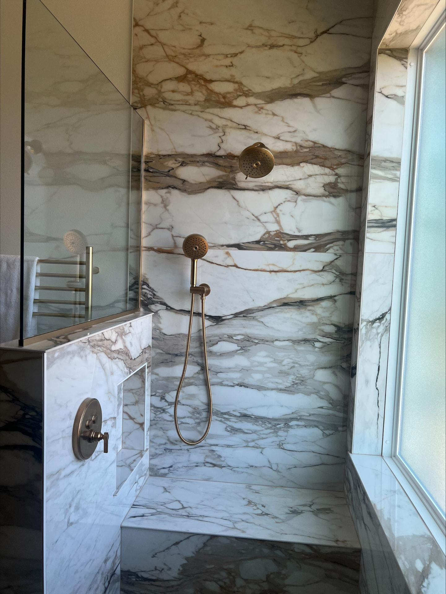 Marble-clad shower with brass rain head, handheld sprayer and a built-in bench
