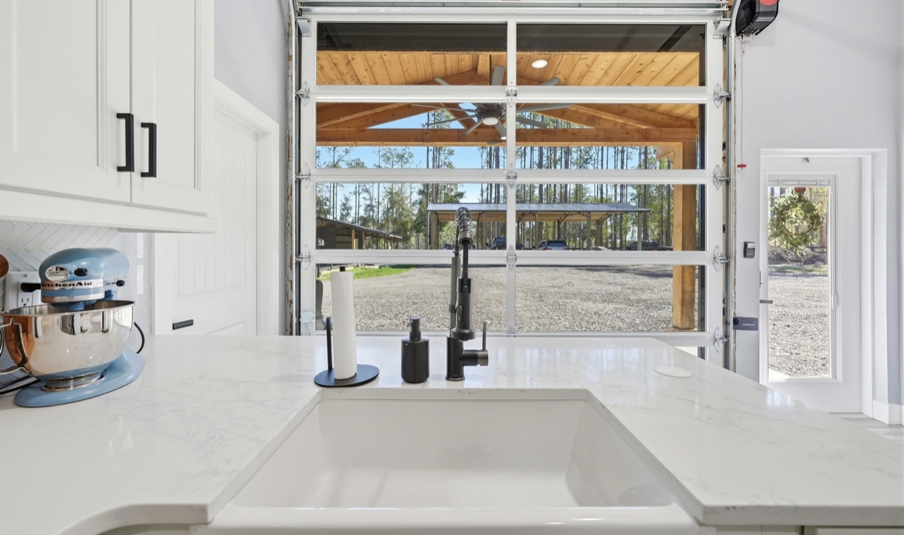 Farmhouse sink and black faucet with a view through the glass garage door to the covered patio