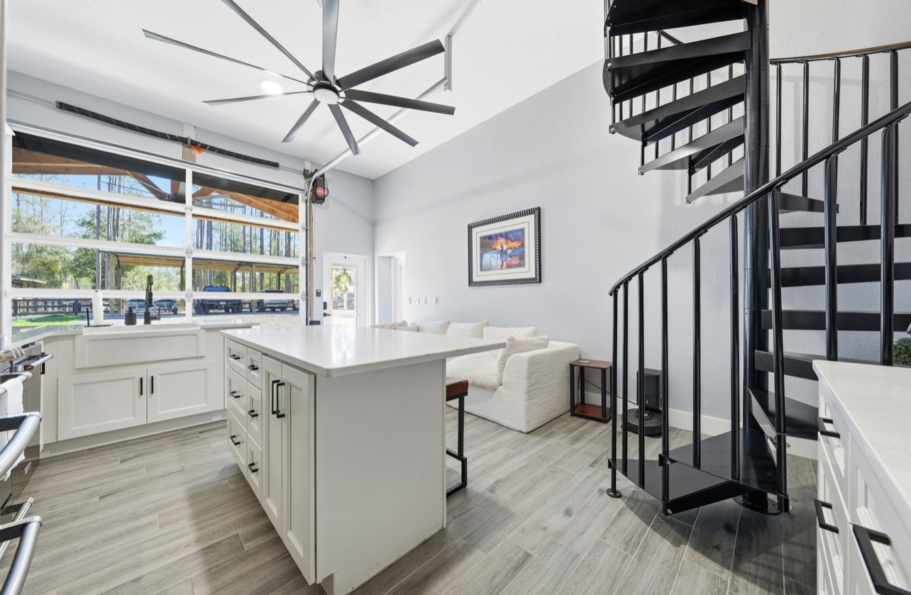 Open kitchen with a large island, farmhouse sink and a black spiral staircase