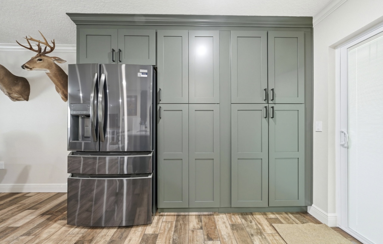 Bank of floor-to-ceiling sage pantry cabinets flanking a stainless refrigerator
