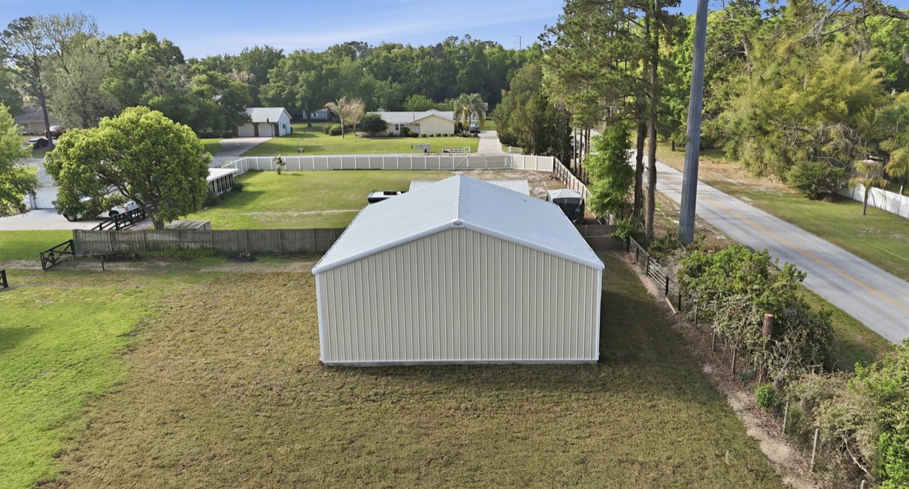 Aerial view of a completed tan metal building with a white standing-seam roof on a fenced lot