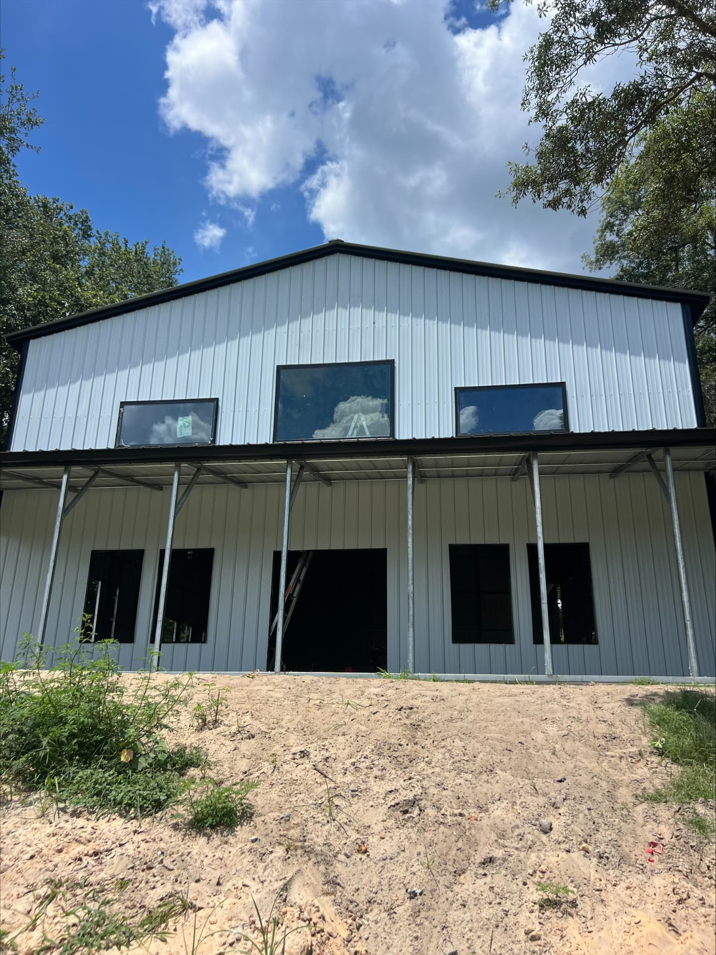 Two-story metal barndominium with wraparound porch and upper-level windows under construction