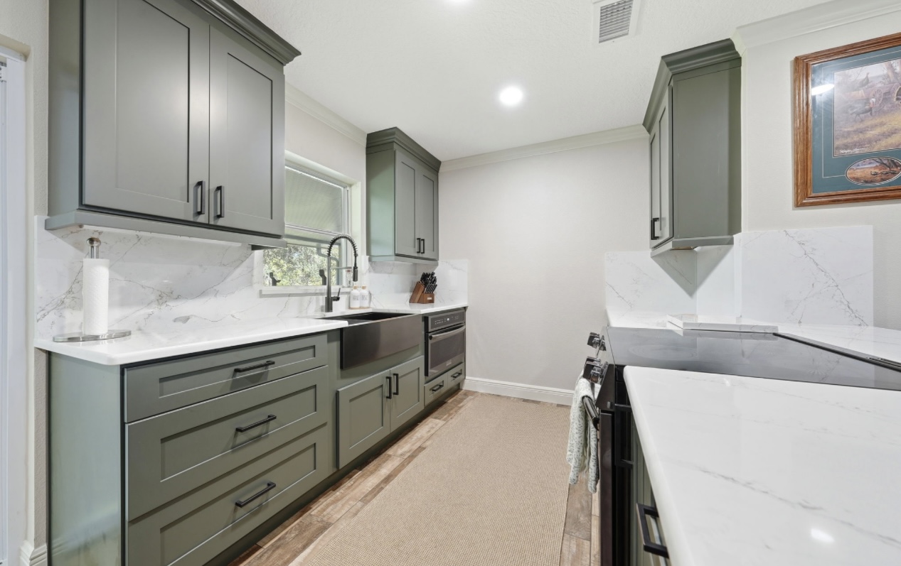 Remodeled galley kitchen with sage green shaker cabinets, quartz counters and a full marble-look backsplash