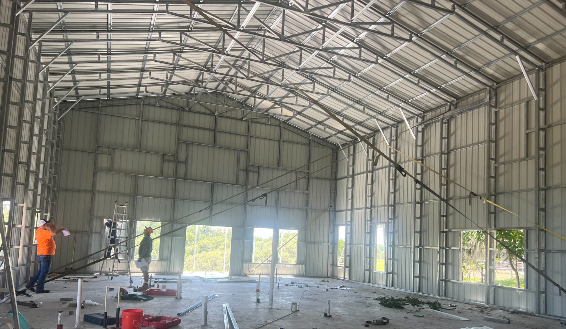Crew working inside a steel building shell with exposed purlins and framed window openings