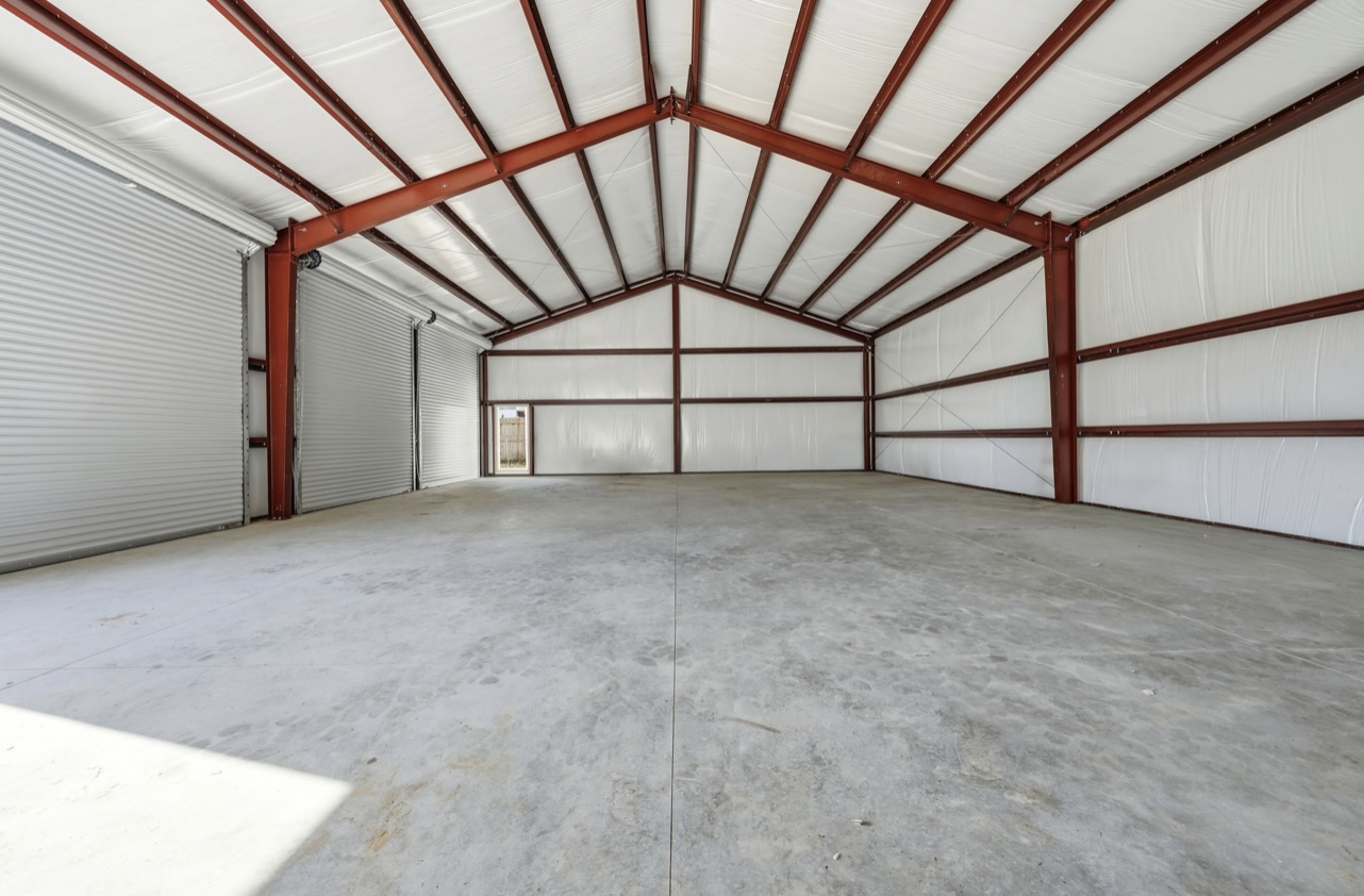 Interior of a red-iron steel workshop with white insulated walls, two roll-up doors and a smooth concrete slab
