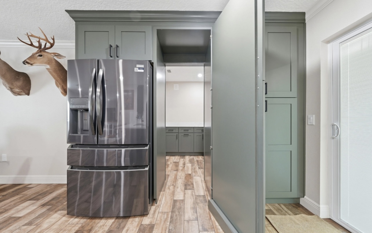 Sage cabinet door opened to reveal a hidden walk-in pantry with counter and cabinets
