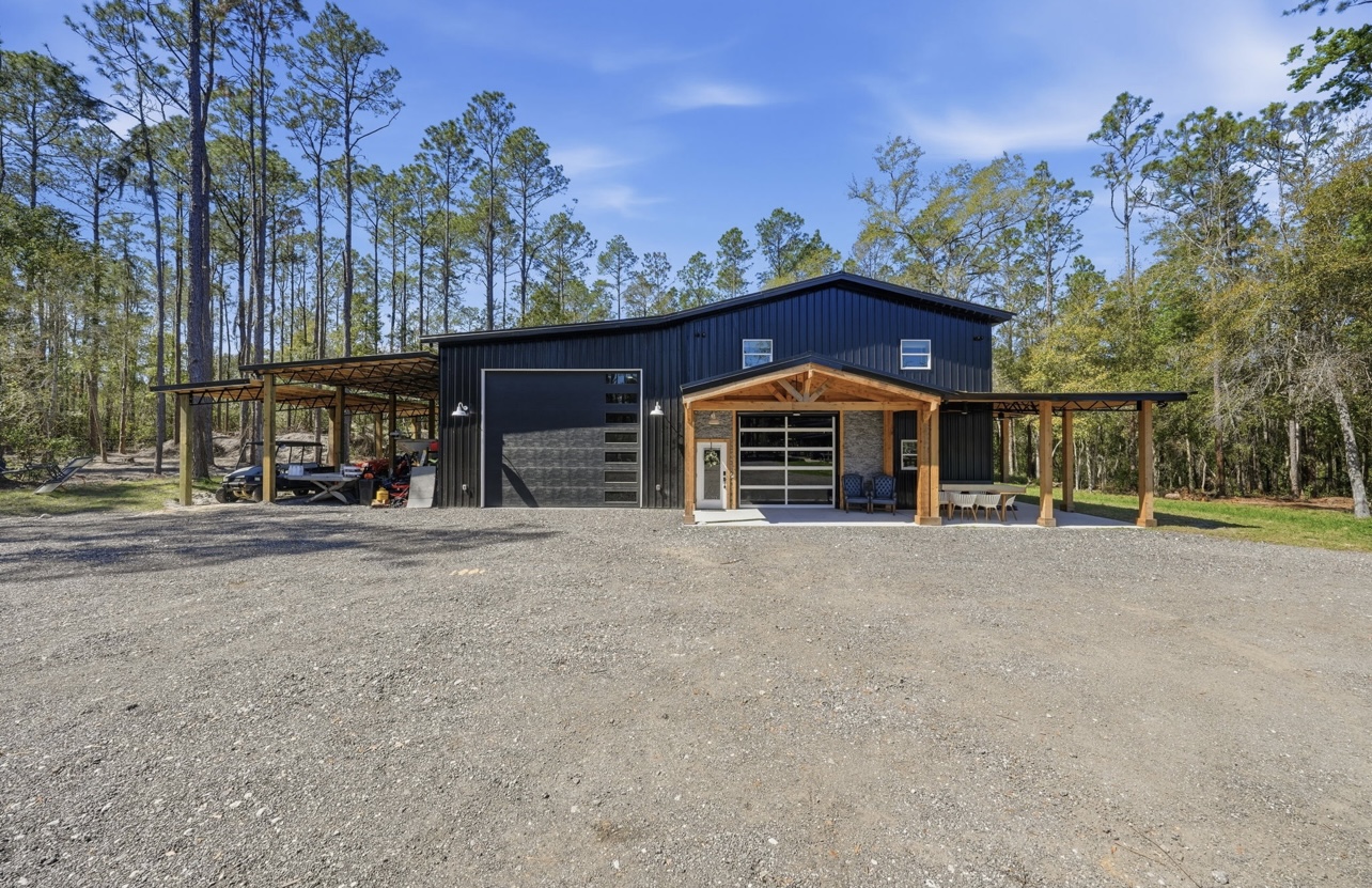 Front elevation of a black metal barndominium with a glass garage door and stone-accented entry