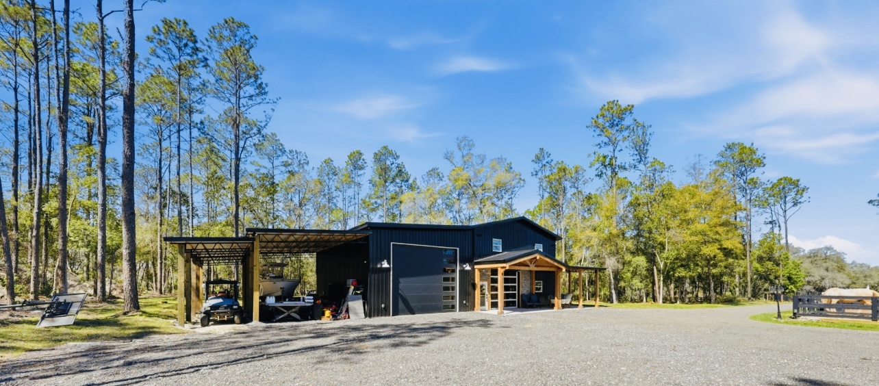 Black metal barndominium with timber-framed porch, equipment lean-to and gravel drive