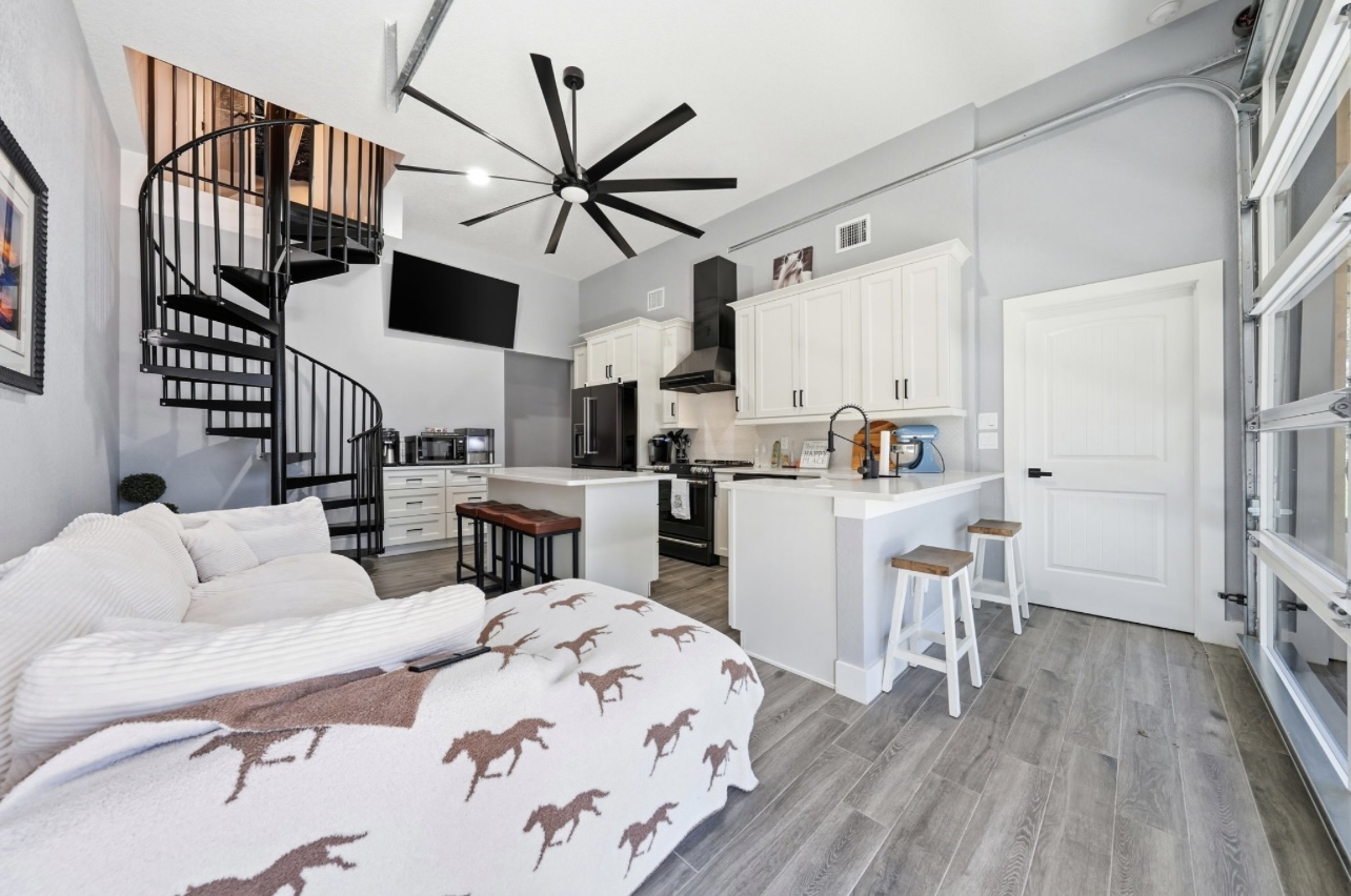 Loft-style living and kitchen space with a black spiral staircase, large fan and sectional sofa