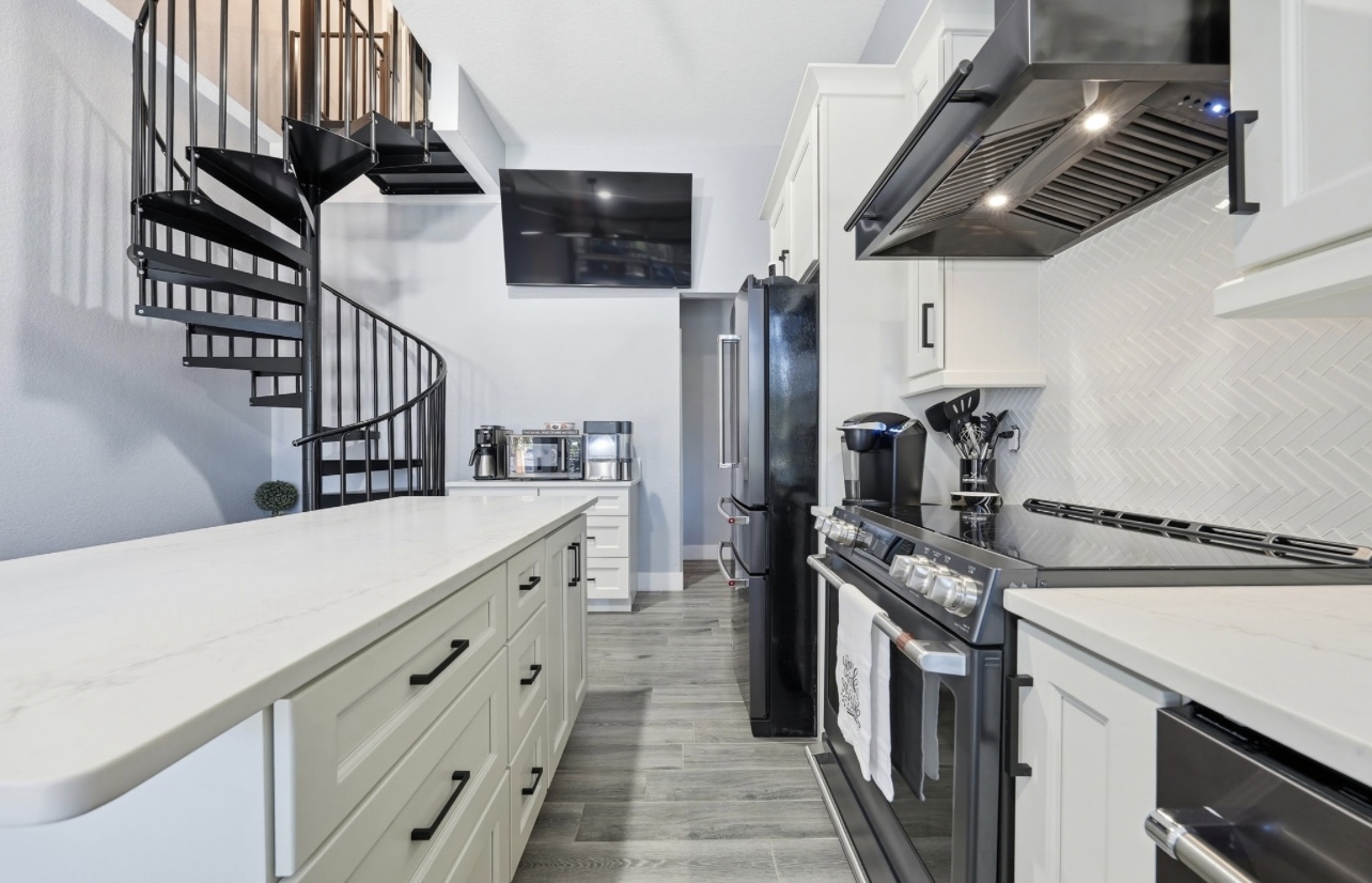 White kitchen with quartz island, herringbone backsplash, stainless hood and black spiral staircase