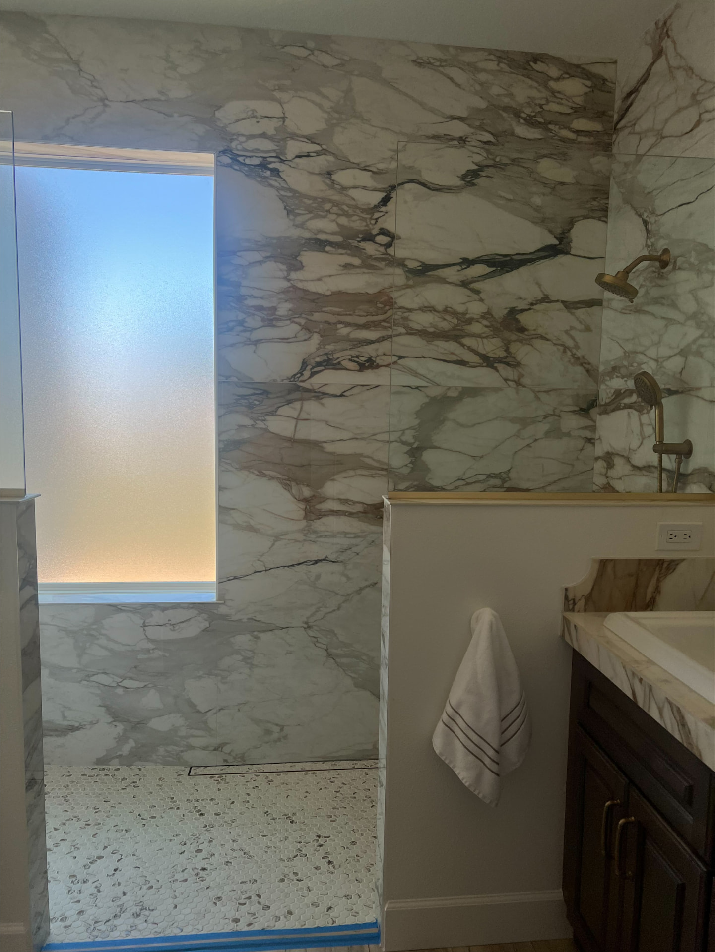 Curbless marble shower with linear drain, penny-round floor tile and a brass shower set
