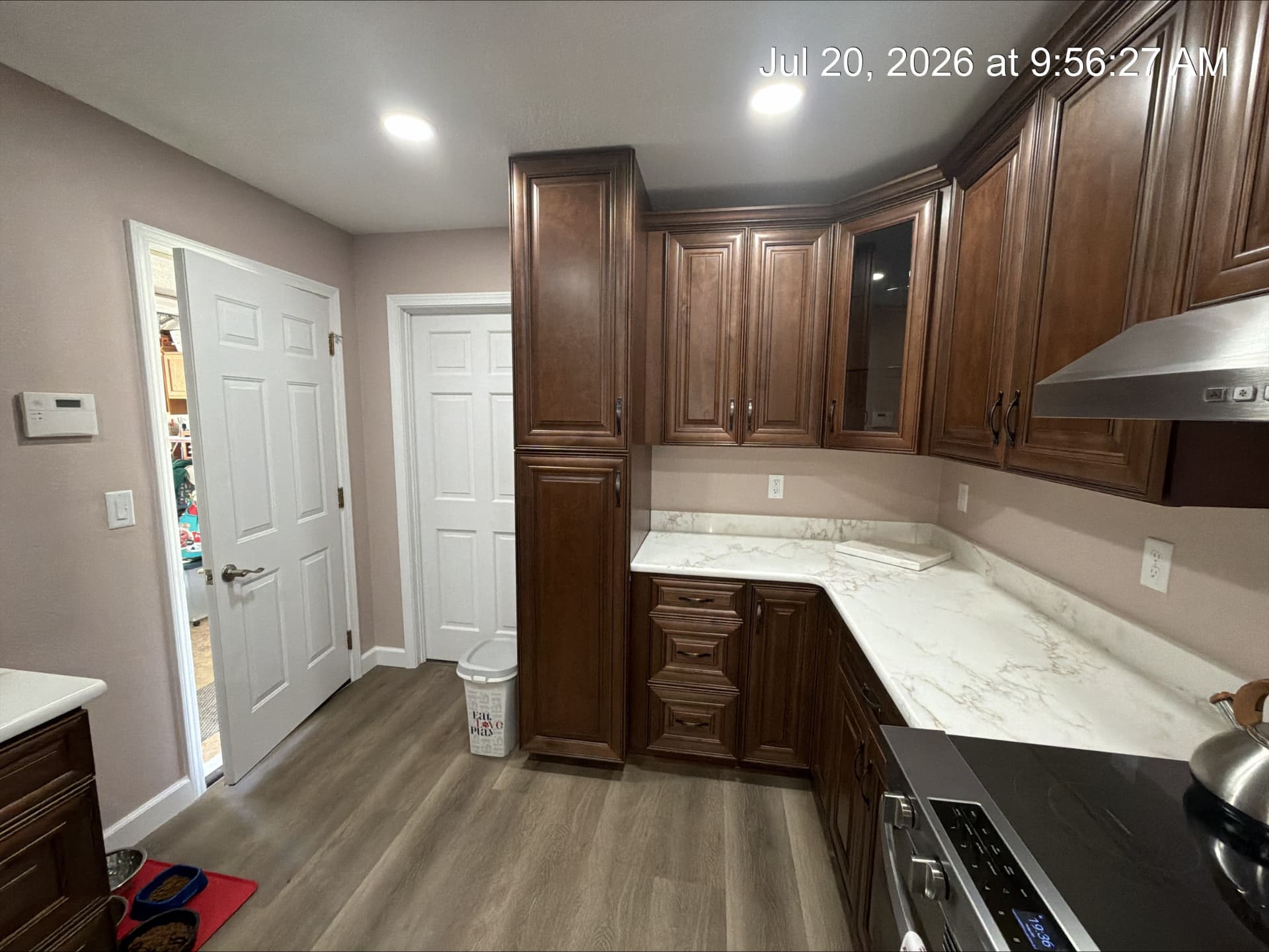 Corner run of walnut cabinetry with marble-look quartz counters and stainless hood