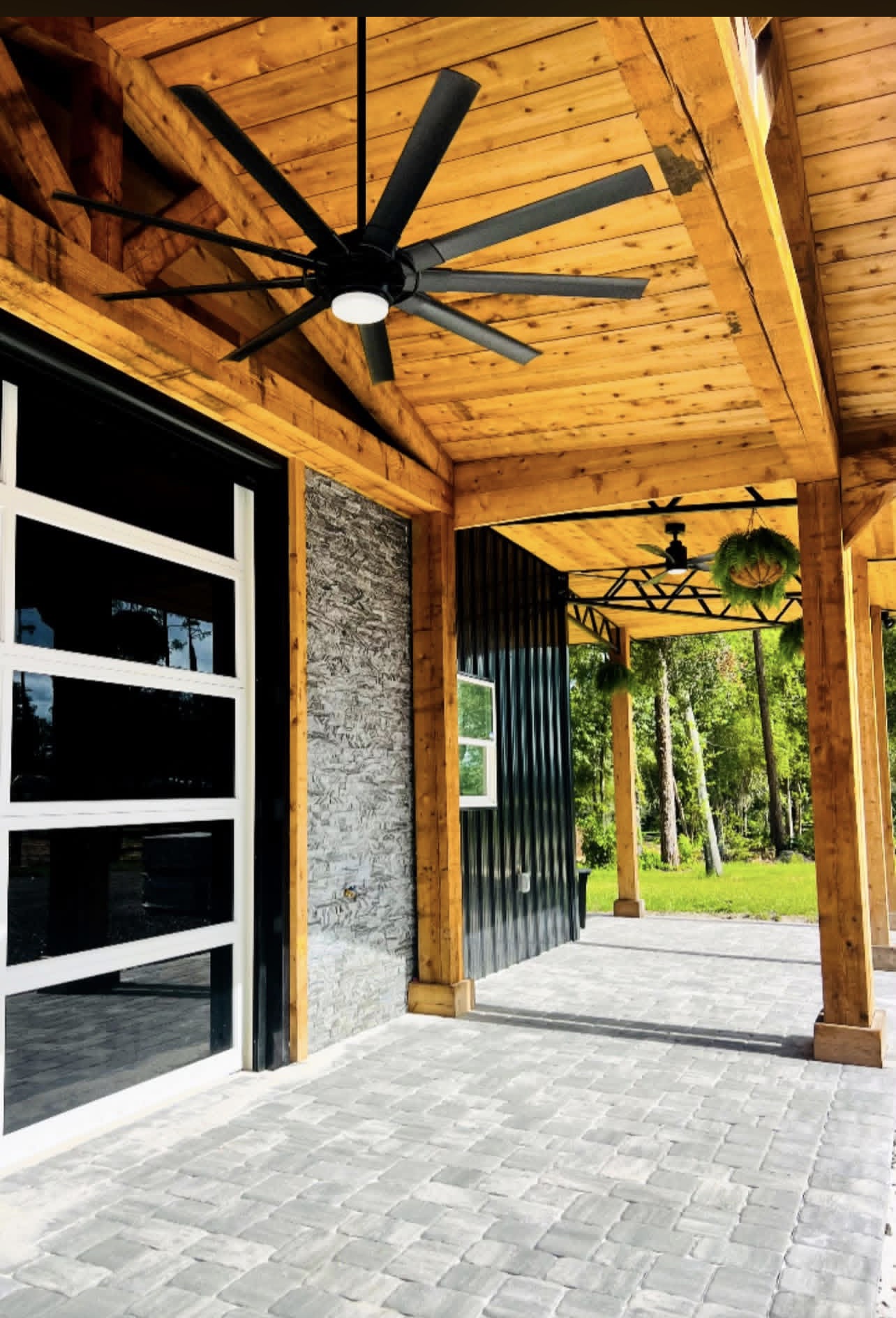 Covered cedar porch with timber beams, black metal siding, stone accent and paver decking