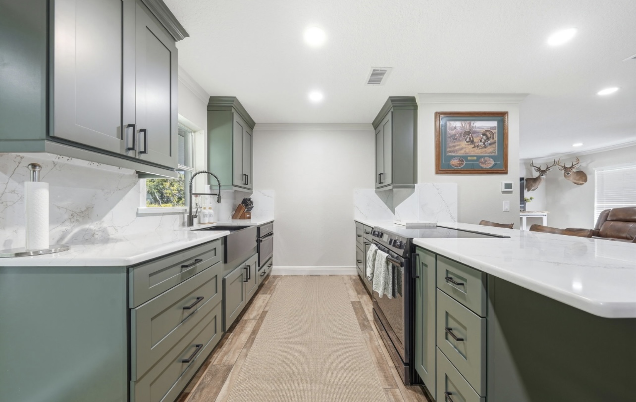 Wide view of a remodeled sage green kitchen with quartz counters and stainless appliances