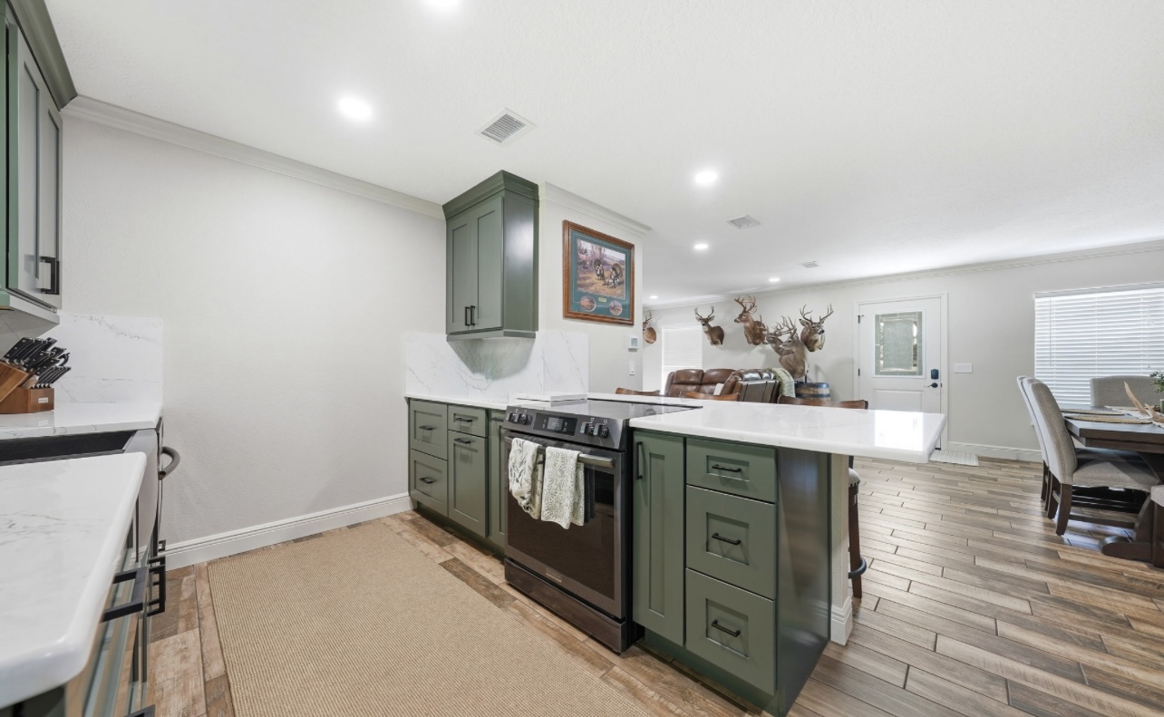 Sage green kitchen peninsula with waterfall quartz counter opening to the living room
