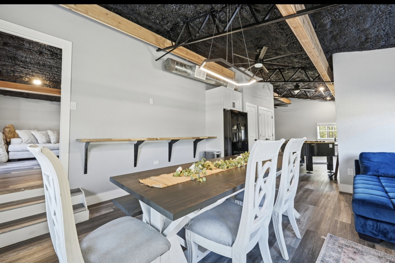 Open dining area with a farmhouse table beneath exposed black trusses and wood beams