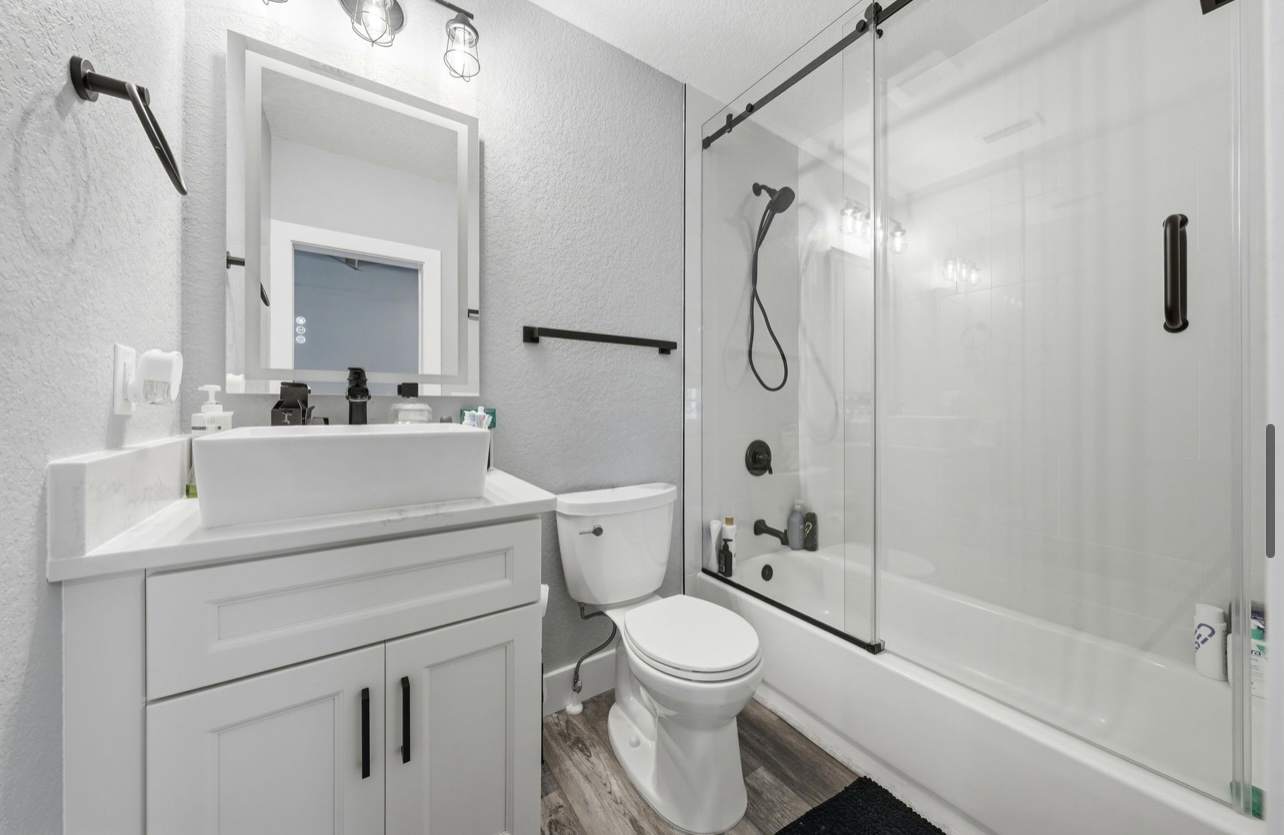 Remodeled bathroom with a vessel sink, backlit mirror and a sliding glass barn-door shower enclosure