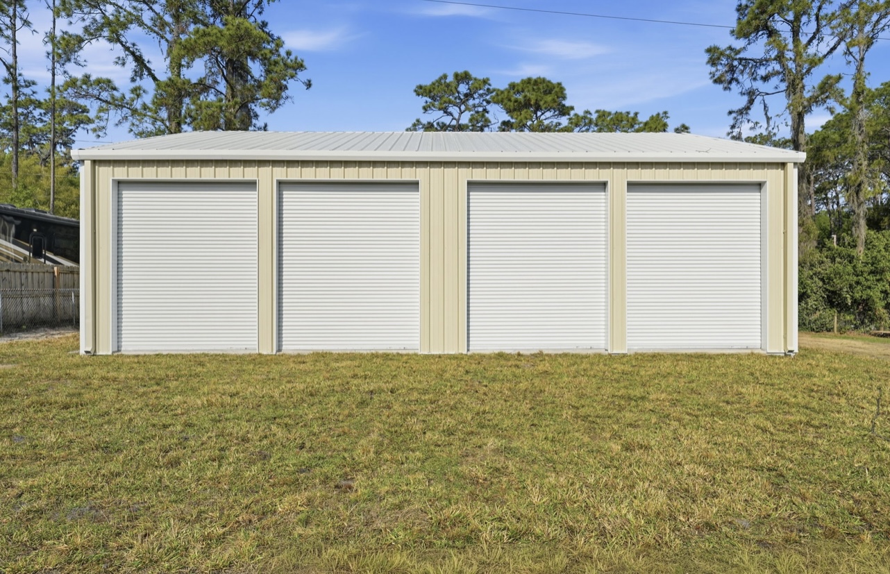 Front elevation of a tan four-bay metal garage with white roll-up doors