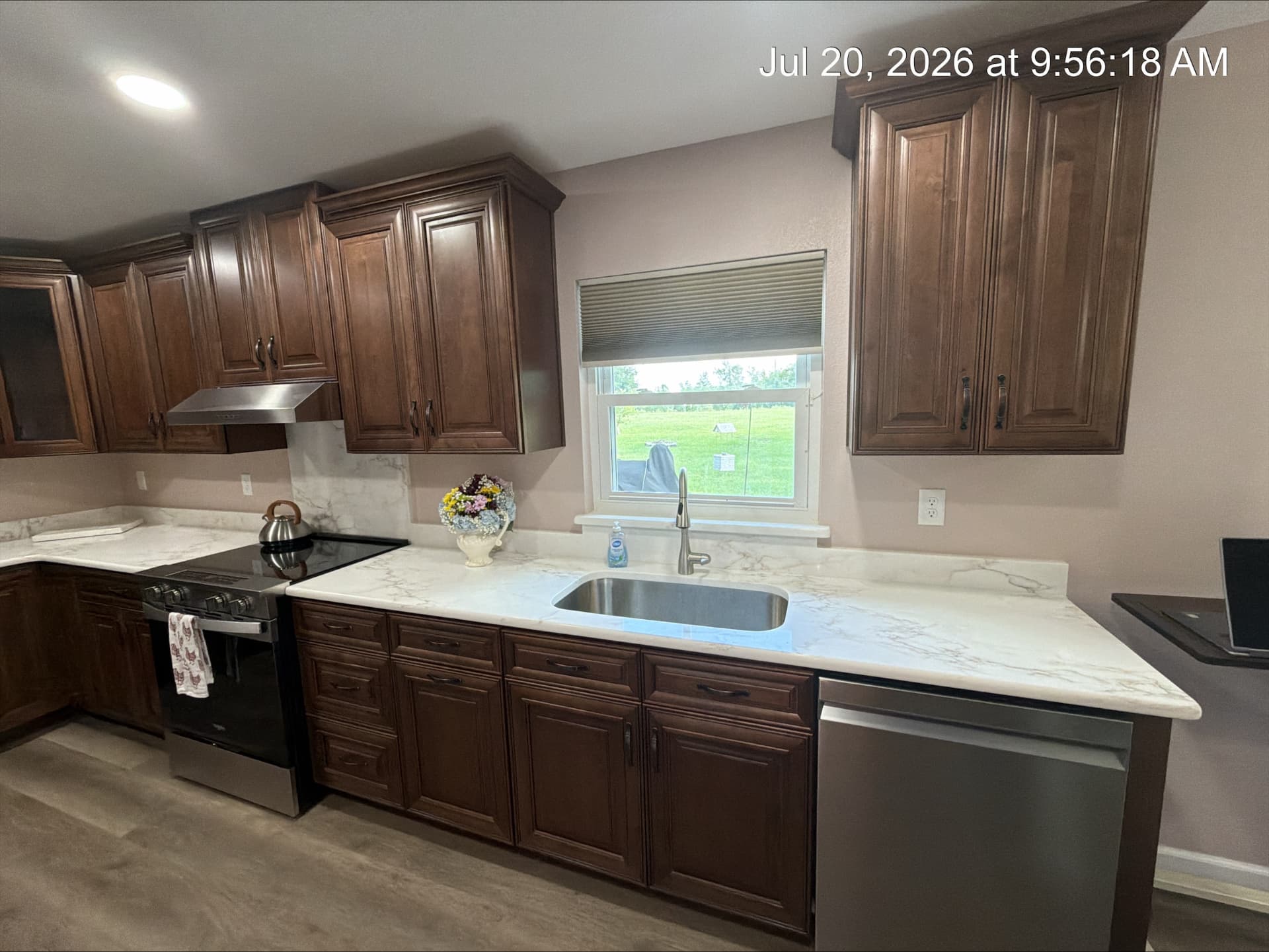 Undermount stainless sink beneath a window with quartz counters and walnut cabinets