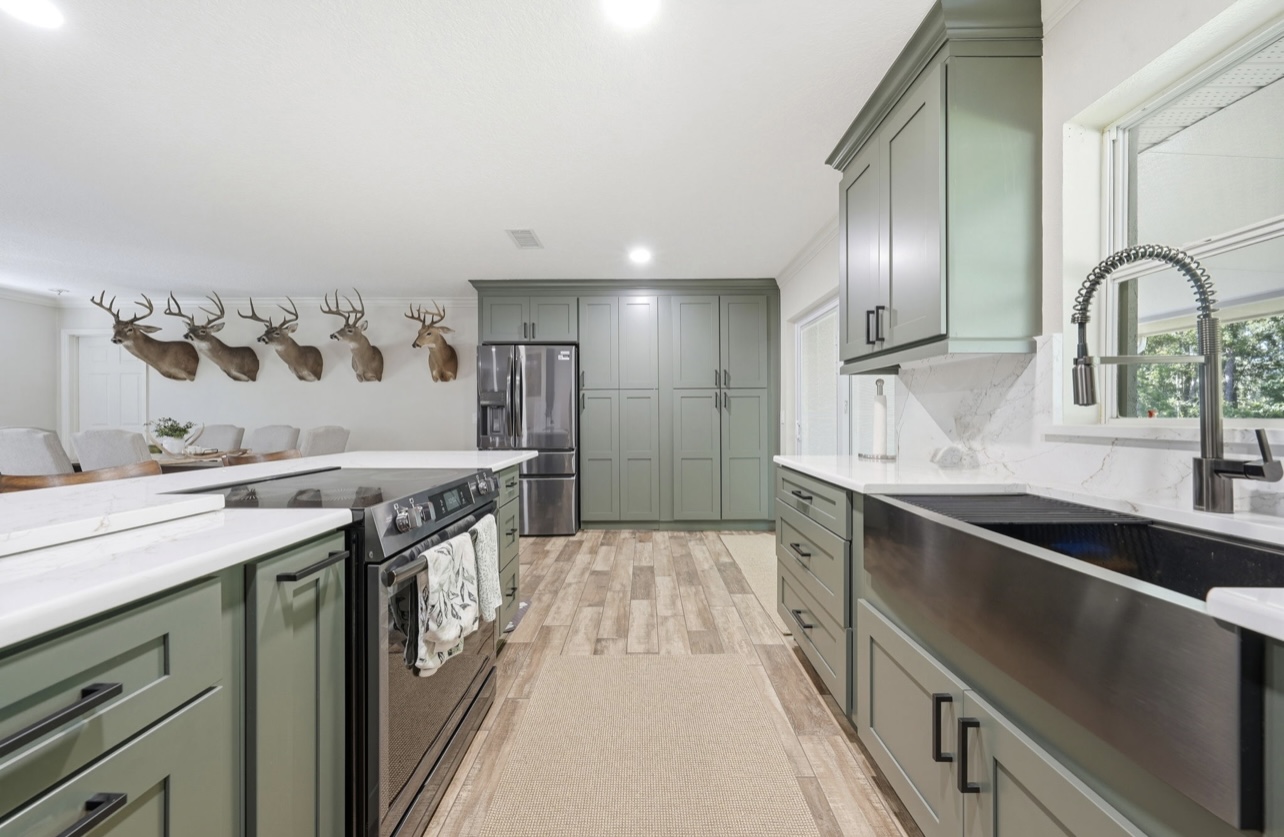 Floor-to-ceiling sage pantry cabinets beside a stainless refrigerator in a remodeled kitchen