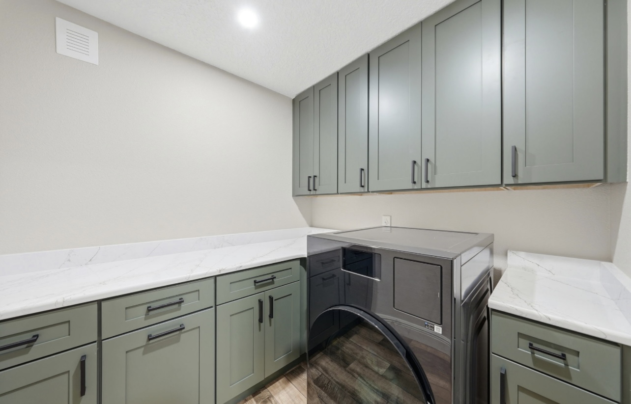Laundry room with sage cabinetry, quartz folding counter and a front-load dryer