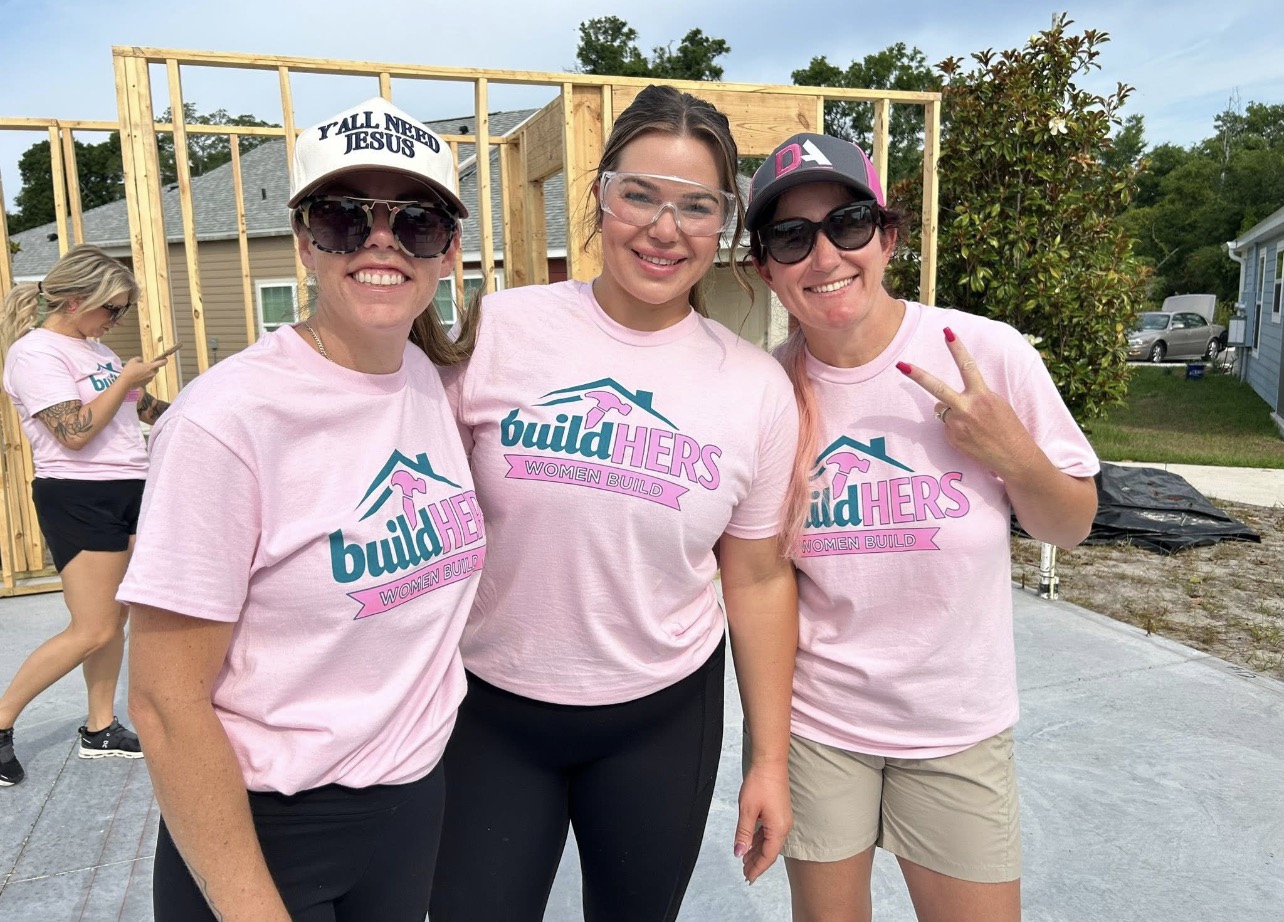 Volunteers in pink buildHERS Women Build shirts on a Habitat for Humanity framing site