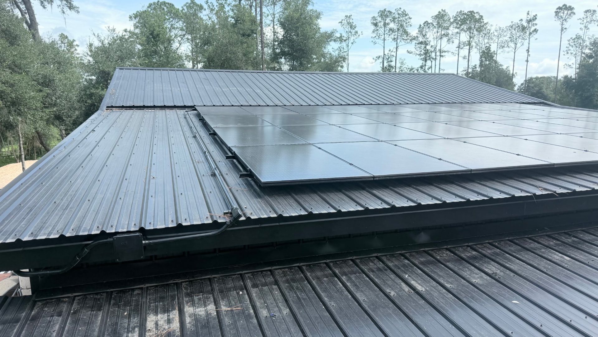 Black solar panel array mounted on a standing seam metal roof surrounded by pines