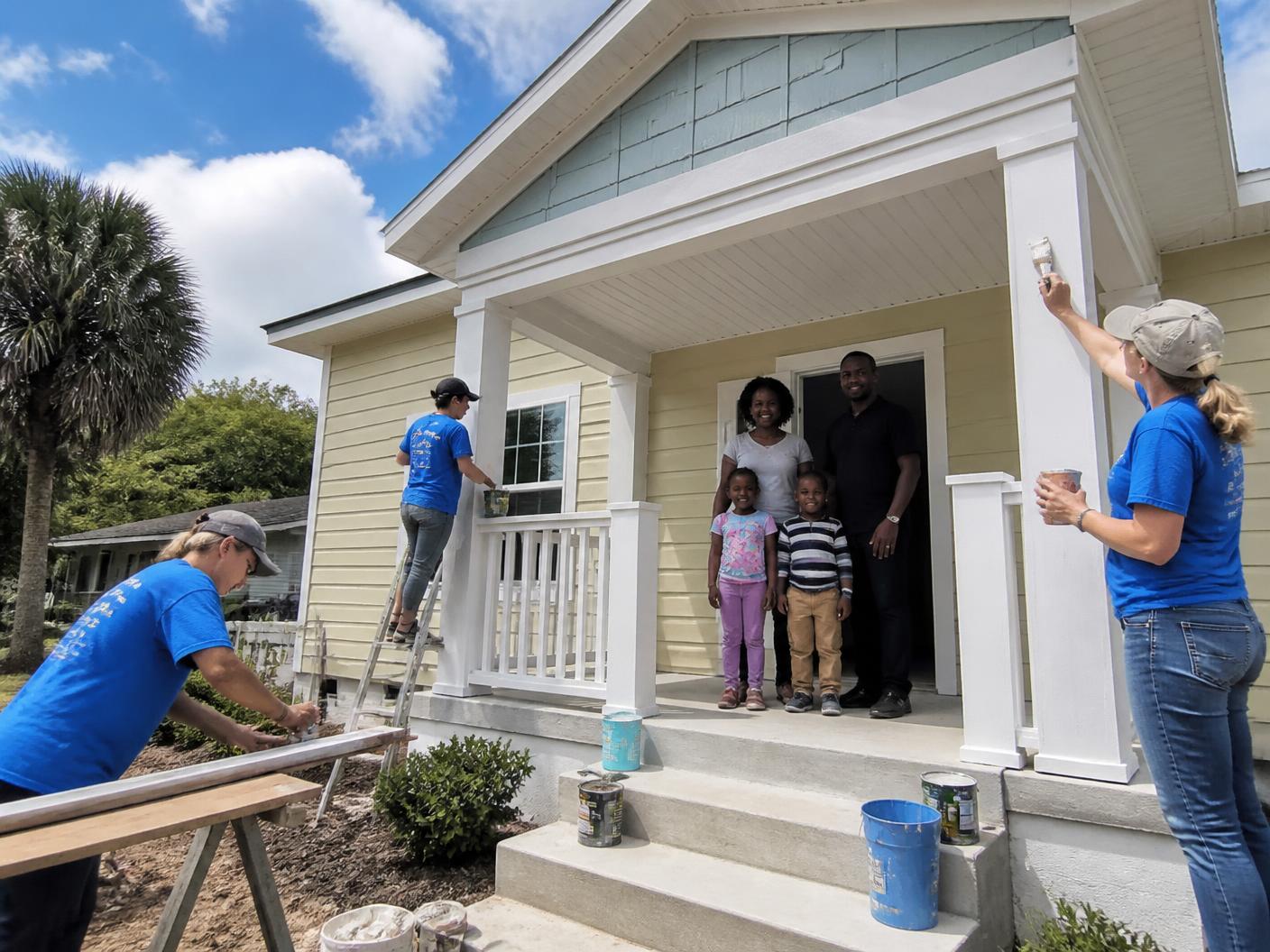 Volunteers painting the porch of a newly built Florida home while the homeowner family stands on the steps