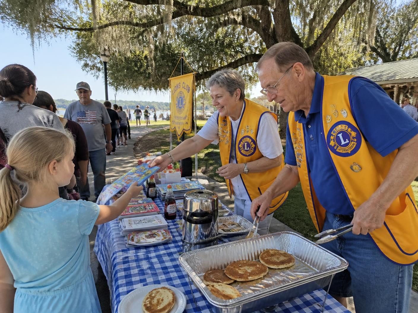 Service club volunteers handing out books and serving breakfast to children at a Central Florida park event